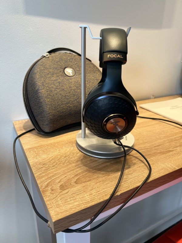 Headphones labeled "Focal" are displayed on a stand, with a carrying case placed beside them on a wooden surface.